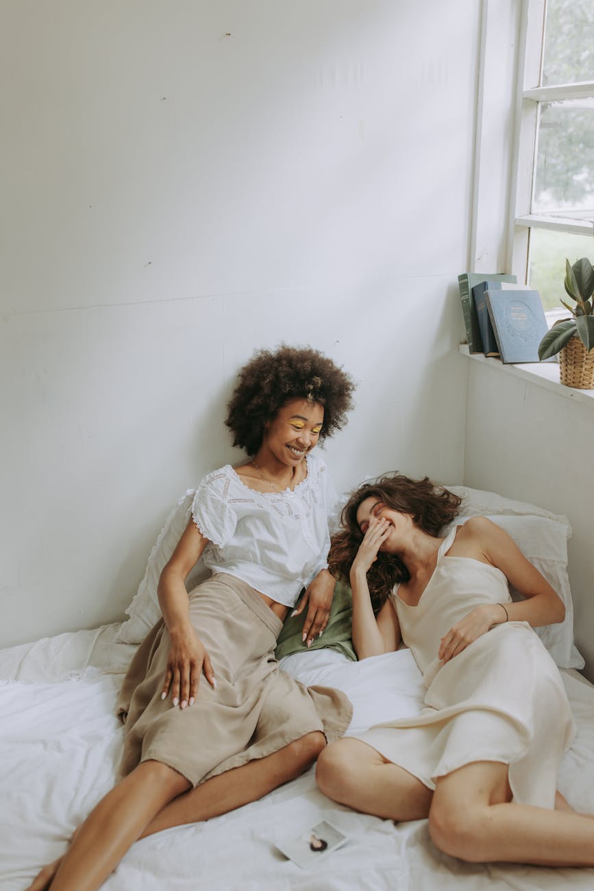 two women talking and laughing while sitting on the bed